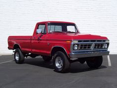 a red truck parked in a parking lot next to a white brick wall with black lettering on it