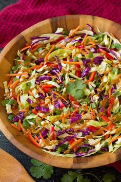 a wooden bowl filled with shredded carrots, cabbage and cilantro on top of a red cloth