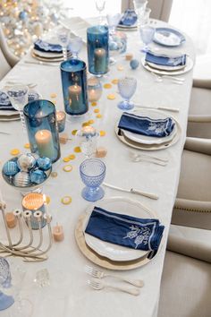 the table is set with blue and white dishes, silverware, candles, and napkins