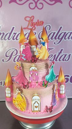 a pink cake with princesses on it sitting on top of a metal stand in front of a sign