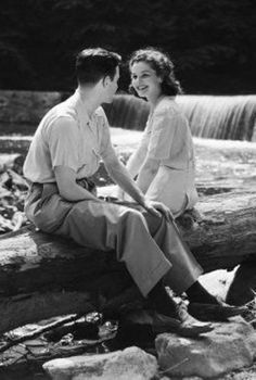 a man and woman sitting on top of a log next to a waterfall