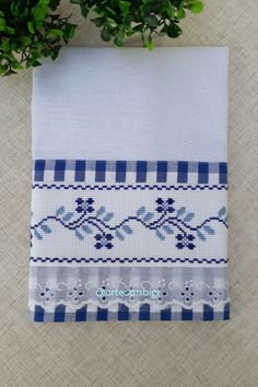 a blue and white cross stitched dish towel next to a potted plant