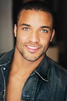 a close up of a person wearing a denim shirt and smiling at the camera with blue eyes