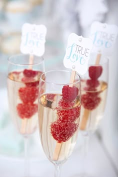 three wine glasses filled with raspberries on top of a white table topped with strawberries