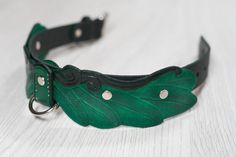 a close up of a green leaf on a black leather collar with metal studs