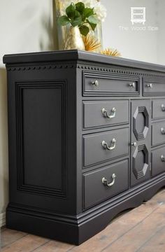 an old dresser is painted black with silver hardware and flowers on top in the corner