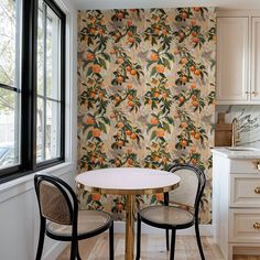 two chairs sitting at a table in front of a wallpapered kitchen with oranges on it