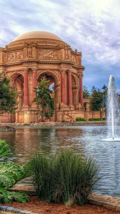 a large building with a fountain in front of it and some plants around the perimeter