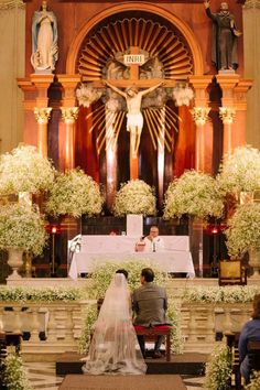 the bride and groom are sitting at the alter in front of the altar with flowers