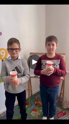 two young boys standing next to each other holding cups