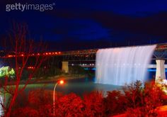 the falls at night are lit up with red lights and trees in front of them