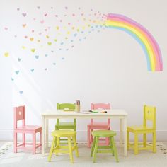 a child's table and chairs in front of a rainbow wall decal