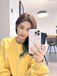 a woman holding up her cell phone in front of her face and wearing a yellow sweatshirt