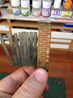 a hand holding a piece of wood that has been placed in front of a brick wall