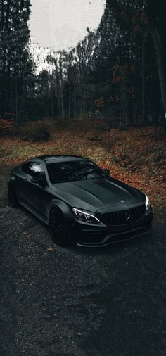 a black sports car parked on the side of a road in front of some trees