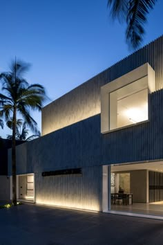 an exterior view of a modern house with palm trees in the foreground and lights on