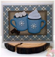 two blue mugs with white snowflakes on them are sitting in front of a wood slice