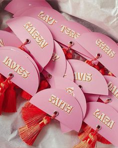 pink tags with gold lettering and tassels on white paper in a pile together