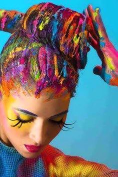 a woman with colorful hair and makeup is holding her hands up to her head while she has