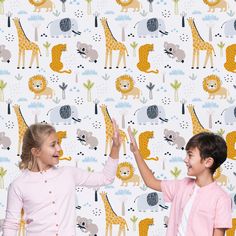 two children standing in front of a wall with giraffes on it