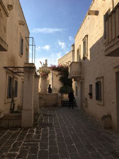 two people are walking down an alleyway between two buildings, one with flowers on it