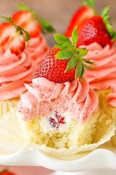 two cupcakes with pink frosting and strawberries on top