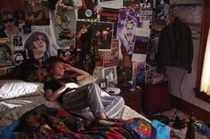 a woman laying in her bed surrounded by posters and other things on the wall behind her