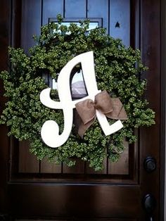 a wreath with the letter j on it hanging from a front door, decorated with greenery