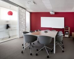 an empty conference room with red walls and white board on the wall, chairs around a table