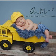 a baby laying on top of a toy truck with a blue blanket and yellow hat