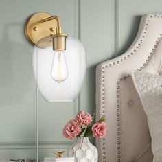 a white bed with pink flowers in a vase next to a light on the wall