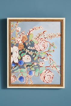 a painting hanging on the wall with flowers painted on it's side and gold frame