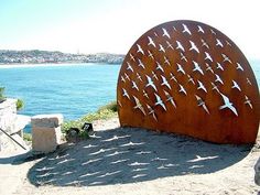 there is a large metal sculpture with birds on it in the sand by the water