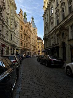 cars parked on the side of a street next to tall buildings with steeple tops