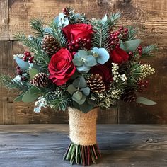 a bouquet of red roses and greenery in a burlock vase on a wooden table