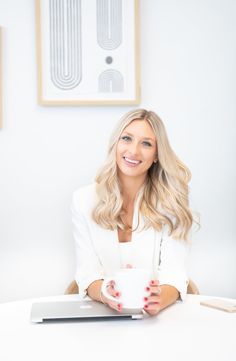 a woman sitting at a table with a laptop and coffee in front of her smiling