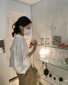 a woman wearing a face mask standing in front of shelves with wine glasses on them