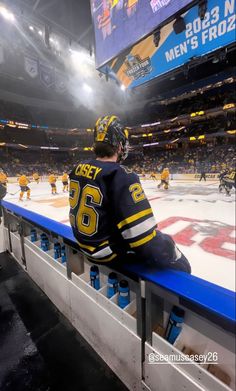 a hockey player is sitting on the bench in front of an ice rink and watching his team play