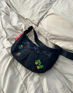 a black purse laying on top of a bed next to a white comforter and pillows