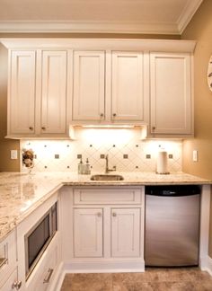 a kitchen with white cabinets and marble counter tops, an oven and dishwasher