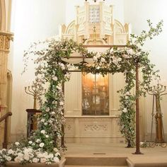 an altar decorated with flowers and greenery in front of a clock on the wall