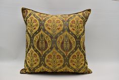 a yellow and green pillow with an intricate design on the front, sitting against a white wall