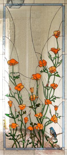 a stained glass window with orange flowers and a blue bird sitting on the ground in front of it