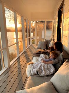 a woman and child sitting on a porch with the sun setting in the distance behind them