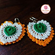 two crocheted earrings with green and white designs on them sitting on a wooden table