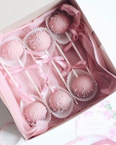 pink cake pops in a box with ribbons and pearls on them are ready to be eaten