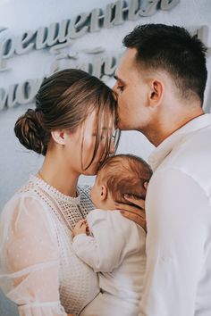 a man and woman kissing their baby in front of a wall with words on it