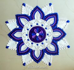 a purple and white doily with a blue flower on the center is hanging from a wall