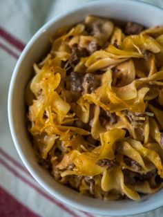 a white bowl filled with pasta and meat on top of a red and white towel