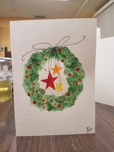 a handmade christmas card with a wreath and stars on it, sitting on a table